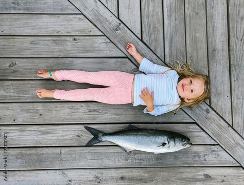 Overhead view of girl lying besides dead fish on pier photo