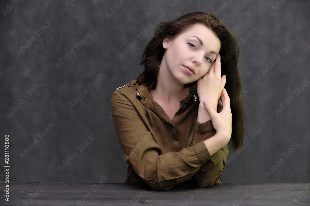 Portrait of a pretty beautiful fashionable adult brunette girl in a dress on a gray background. Sits at the table, talking, bored, showing different poses and emotions Portrait of a pretty beautiful fashionable adult brunette girl in a dress on a gray background. Sits at the table, talking, bored, showing different poses and emotions