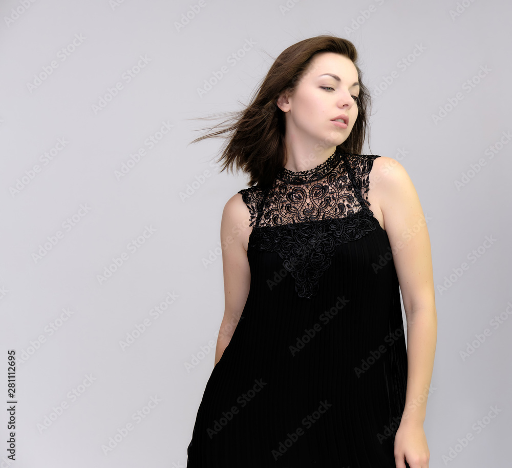 A portrait above the knee of a pretty beautiful fashionable adult brunette girl in a black dress on a white background. Standing right in front of the camera, showing different poses and emotions.