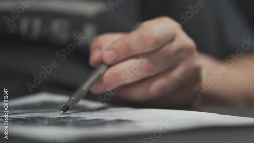 Male hand draws on white paper with a ballpoint pen. Under the light of a desk lamp