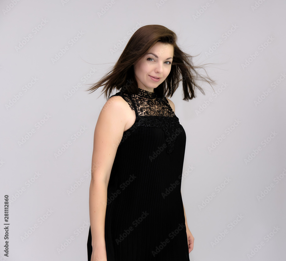 A portrait above the knee of a pretty beautiful fashionable adult brunette girl in a black dress on a white background. Standing right in front of the camera, showing different poses and emotions. A portrait above the knee of a pretty beautiful fashionable adult brunette girl in a black dress on a white background. Standing right in front of the camera, showing different poses and emotions.