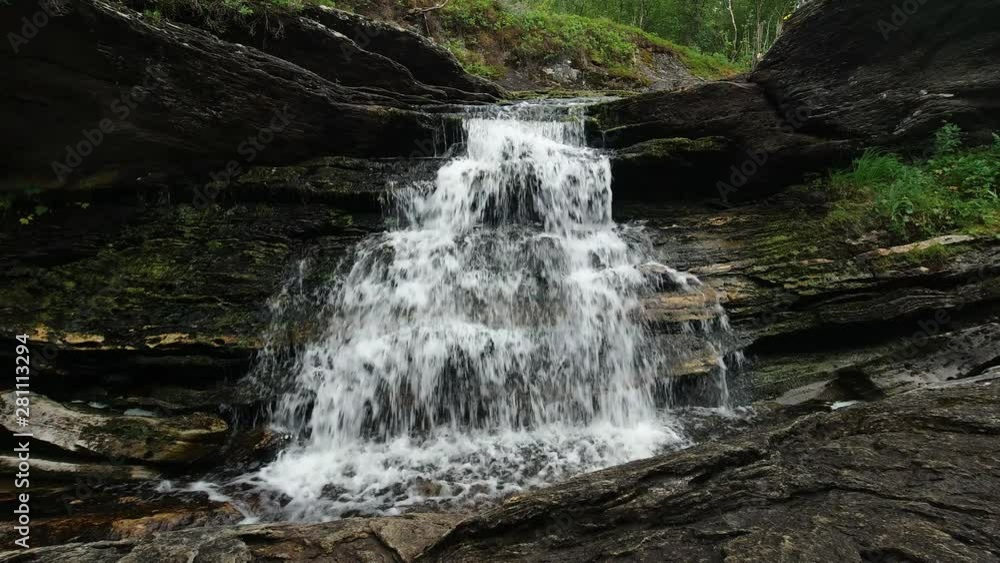 Low angle shot of a waterfall on rocks flowing down in a mossy, wet environment in a forest