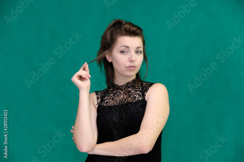 Portrait of a pretty beautiful fashionable adult brunette girl in a black dress on a green background. Standing right in front of the camera, showing different poses and emotions. © Вячеслав Чичаев