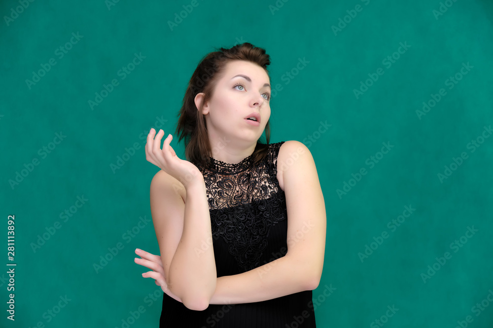 Portrait of a pretty beautiful fashionable adult brunette girl in a black dress on a green background. Standing right in front of the camera, showing different poses and emotions. Portrait of a pretty beautiful fashionable adult brunette girl in a black dress on a green background. Standing right in front of the camera, showing different poses and emotions.