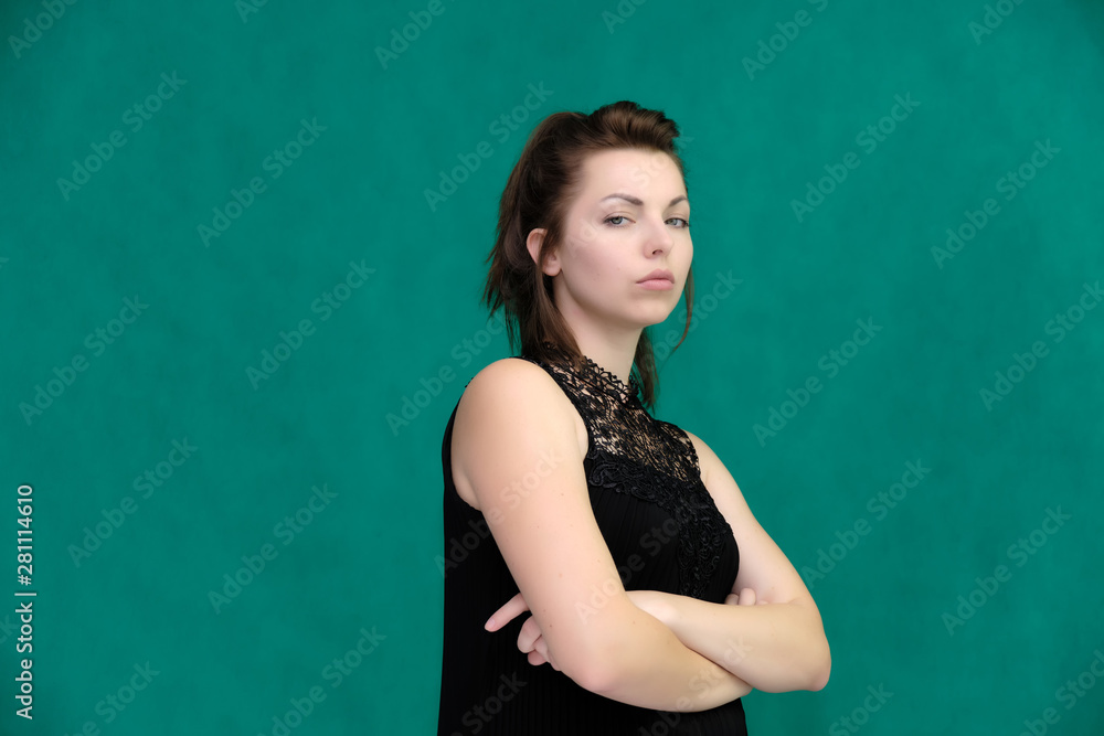 Portrait of a pretty beautiful fashionable adult brunette girl in a black dress on a green background. Standing right in front of the camera, showing different poses and emotions. Portrait of a pretty beautiful fashionable adult brunette girl in a black dress on a green background. Standing right in front of the camera, showing different poses and emotions.