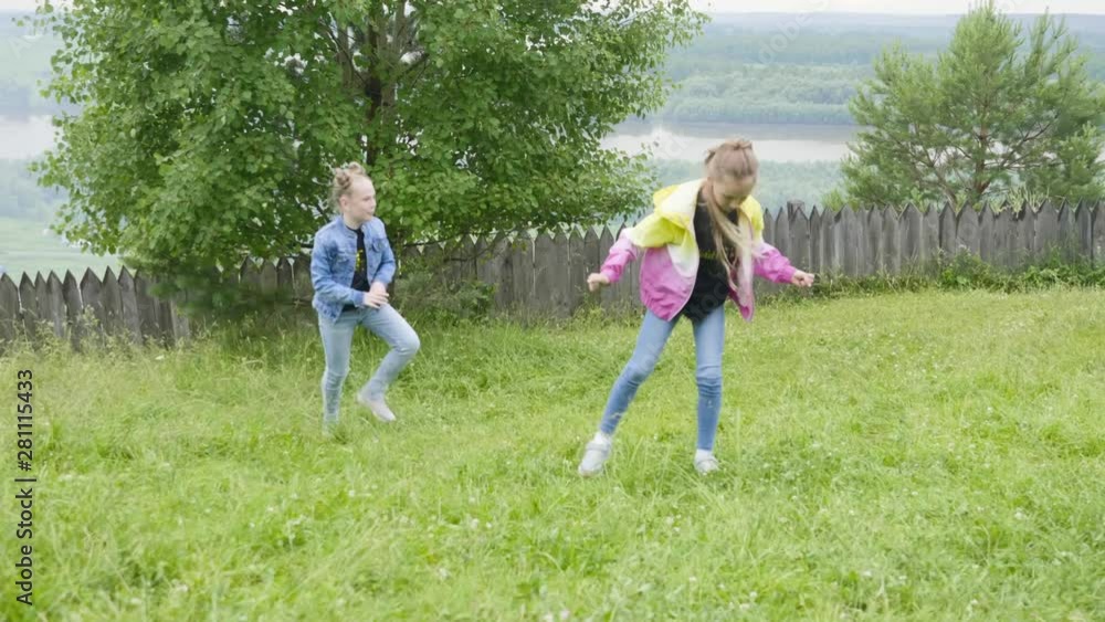 Having a fun time in countryside. Two teen girls making acrobatic cartwheel on lawn walking on nature together. Beautiful foresr and river background. Children sport outdoor activities. Having a fun time in countryside. Two teen girls making acrobatic cartwheel on lawn walking on nature together. Beautiful foresr and river background. Children sport outdoor activities.