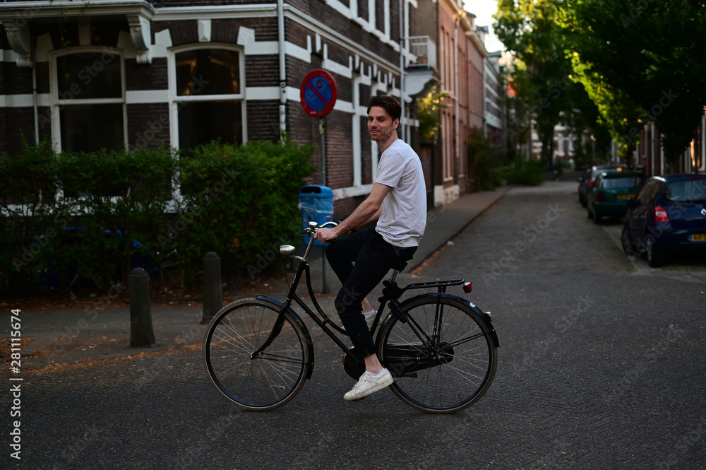 Relaxed and friendly male student riding his bicycle through an old Dutch city with a lot of students