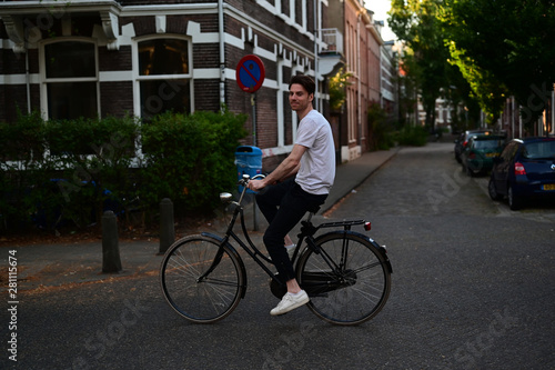 Relaxed and friendly male student riding his bicycle through an old Dutch city with a lot of students