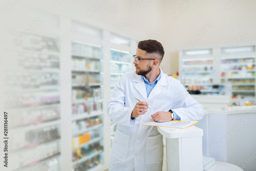 Serious bearded chemist checking assortment of medicine Serious bearded chemist checking assortment of medicine