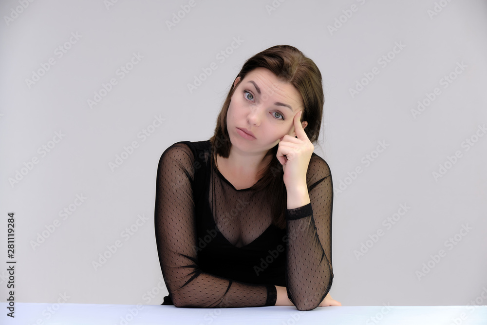 Portrait of a pretty beautiful fashionable adult girl with beautiful brunette hair in a black dress. Sits at the table directly in front of camera, talking demonstrating different poses and emotions Portrait of a pretty beautiful fashionable adult girl with beautiful brunette hair in a black dress. Sits at the table directly in front of camera, talking demonstrating different poses and emotions