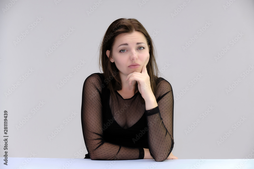 Portrait of a pretty beautiful fashionable adult girl with beautiful brunette hair in a black dress. Sits at the table directly in front of camera, talking demonstrating different poses and emotions Portrait of a pretty beautiful fashionable adult girl with beautiful brunette hair in a black dress. Sits at the table directly in front of camera, talking demonstrating different poses and emotions