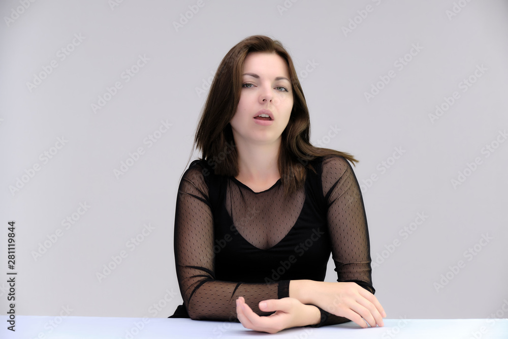 Portrait of a pretty beautiful fashionable adult girl with beautiful brunette hair in a black dress. Sits at the table directly in front of camera, talking demonstrating different poses and emotions Portrait of a pretty beautiful fashionable adult girl with beautiful brunette hair in a black dress. Sits at the table directly in front of camera, talking demonstrating different poses and emotions