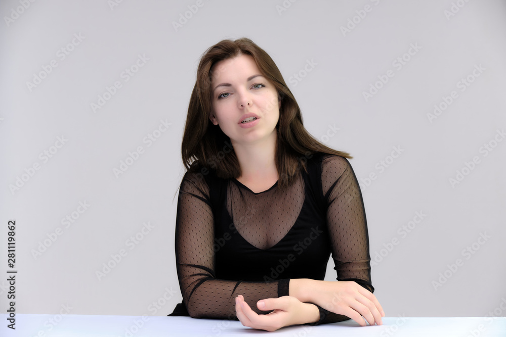 Portrait of a pretty beautiful fashionable adult girl with beautiful brunette hair in a black dress. Sits at the table directly in front of camera, talking demonstrating different poses and emotions Portrait of a pretty beautiful fashionable adult girl with beautiful brunette hair in a black dress. Sits at the table directly in front of camera, talking demonstrating different poses and emotions