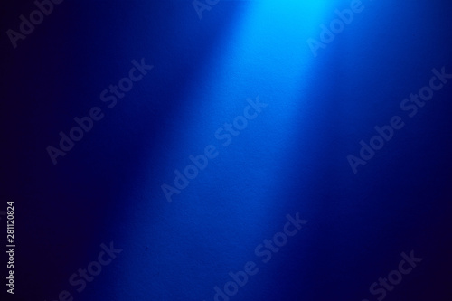 On a dark blue finely textured background, a blue beam of light shines from above