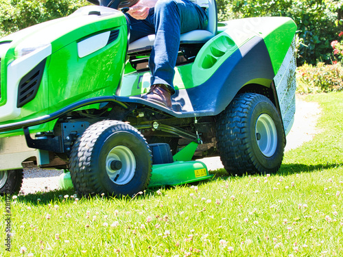 Senior man driving a tractor lawn mower in garden with flowers photo