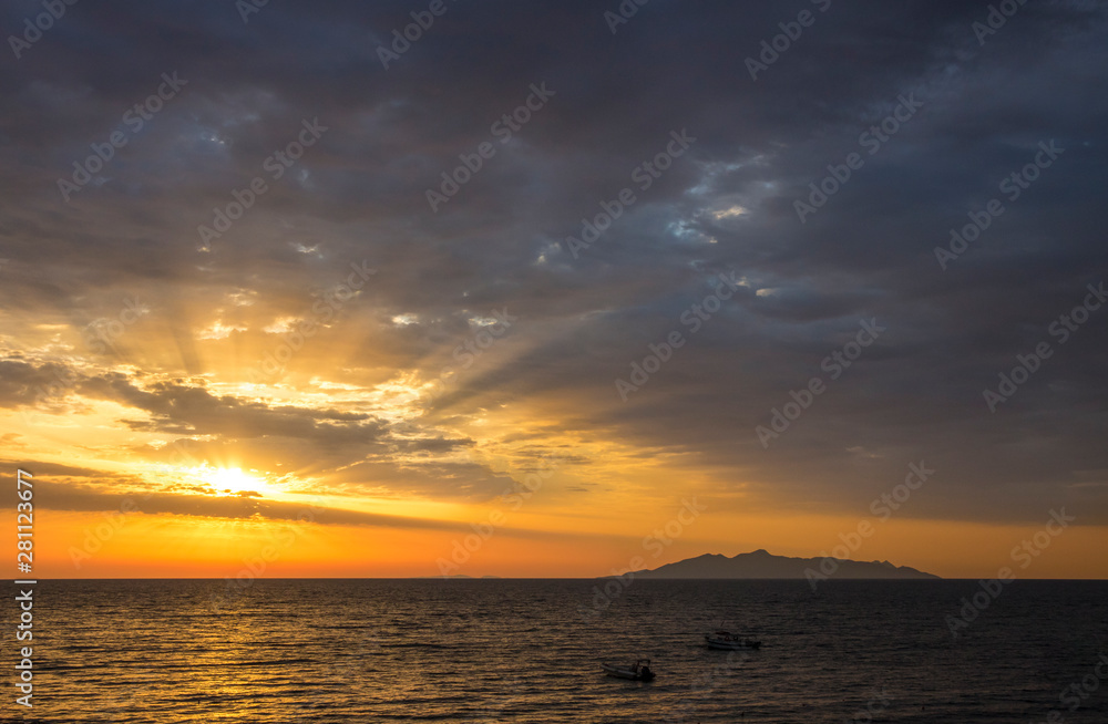 Sunrise from Aegean sea, magical sun rays shining though clouds, silhouette of volcanic island( Anafi, Greece, seen from  Santorini island) on the background. Fresh beginning start concept.