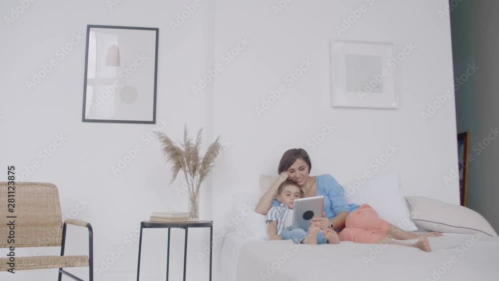 Happy young mother showing cartoon on digital tablet to her toddler son before going to sleep. Happy mother showing cartoon on digital tablet to her toddler son. Happy young mother showing cartoon on digital tablet to her toddler son before going to sleep. Happy mother showing cartoon on digital tablet to her toddler son.