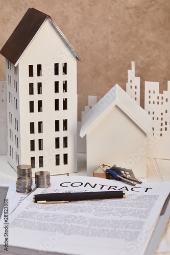 houses models on white wooden table with contract, keys and coins, real estate concept photo