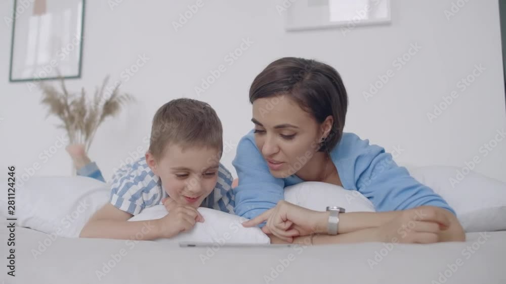Happy young mother showing cartoon on digital tablet to her toddler son before going to sleep. Happy mother showing cartoon on digital tablet to her toddler son. Happy young mother showing cartoon on digital tablet to her toddler son before going to sleep. Happy mother showing cartoon on digital tablet to her toddler son.