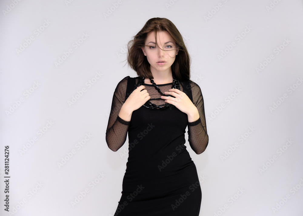 Portrait on white background of a pretty slim beautiful fashionable adult girl with beautiful brunette hair in a black dress. Standing talking demonstrating different poses and emotions Portrait on white background of a pretty slim beautiful fashionable adult girl with beautiful brunette hair in a black dress. Standing talking demonstrating different poses and emotions