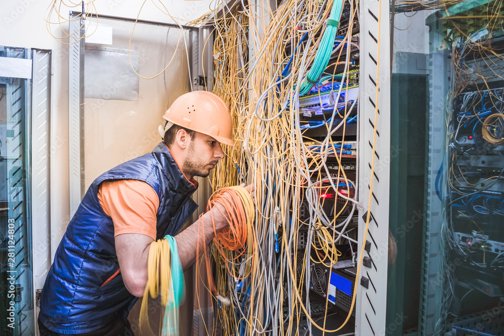 A technician commutes many trouble-free wires in the data center server  room. Engineer repair broken internet connection. A professional internet  campaign worker serves a rack with a central route. Stock Photo
