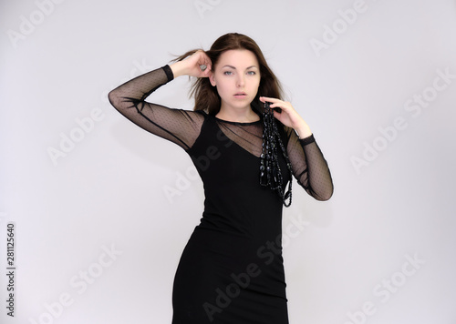 Portrait on white background of a pretty slim beautiful fashionable adult girl with beautiful brunette hair in a black dress. Standing talking demonstrating different poses and emotions © Вячеслав Чичаев
