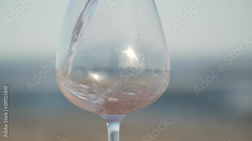 rose wine is poured from a bottle into a glass against the background of the sea and the beach