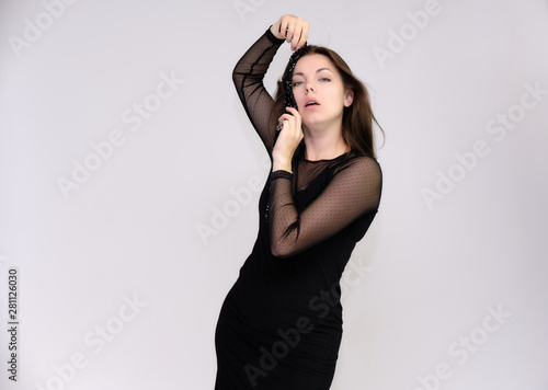 Portrait on white background of a pretty slim beautiful fashionable adult girl with beautiful brunette hair in a black dress. Standing talking demonstrating different poses and emotions © Вячеслав Чичаев