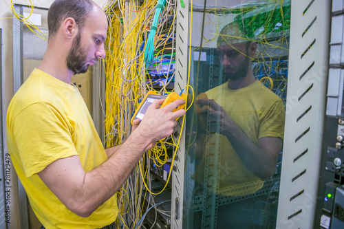 The system administrator is testing the network with a reflectometer.  The man works in the server room of the datacenter. A technician measures the signal level in a fiber optic cable. photo