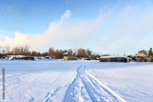 Road on snow and ice of frozen lake, tracks going to village, sunny cold weather