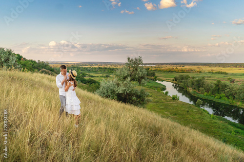 Young couple are happy and standing on a meadow in the evening on summer season. The river on background.