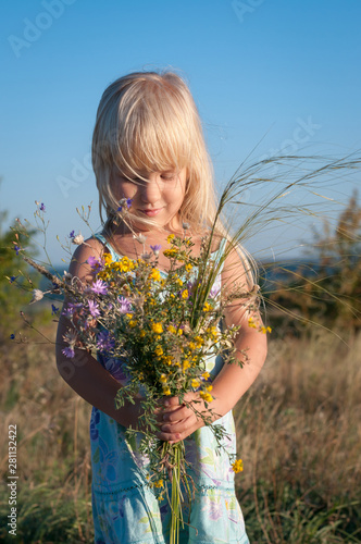 Little cute blonde girl in a field on a sunny day with a bouquet of wild flowers.