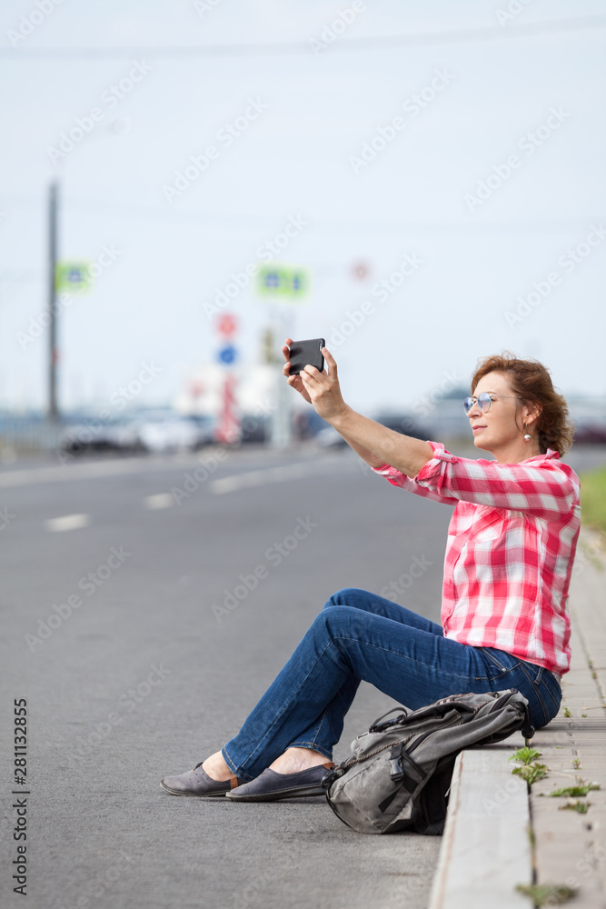 Attractive woman blogging with smartphone while sitting road border in city, an empty highway Attractive woman blogging with smartphone while sitting road border in city, an empty highway