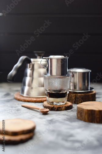 Making Vietnamese drip coffee with condensed milk in phin on wood slabs on dark background