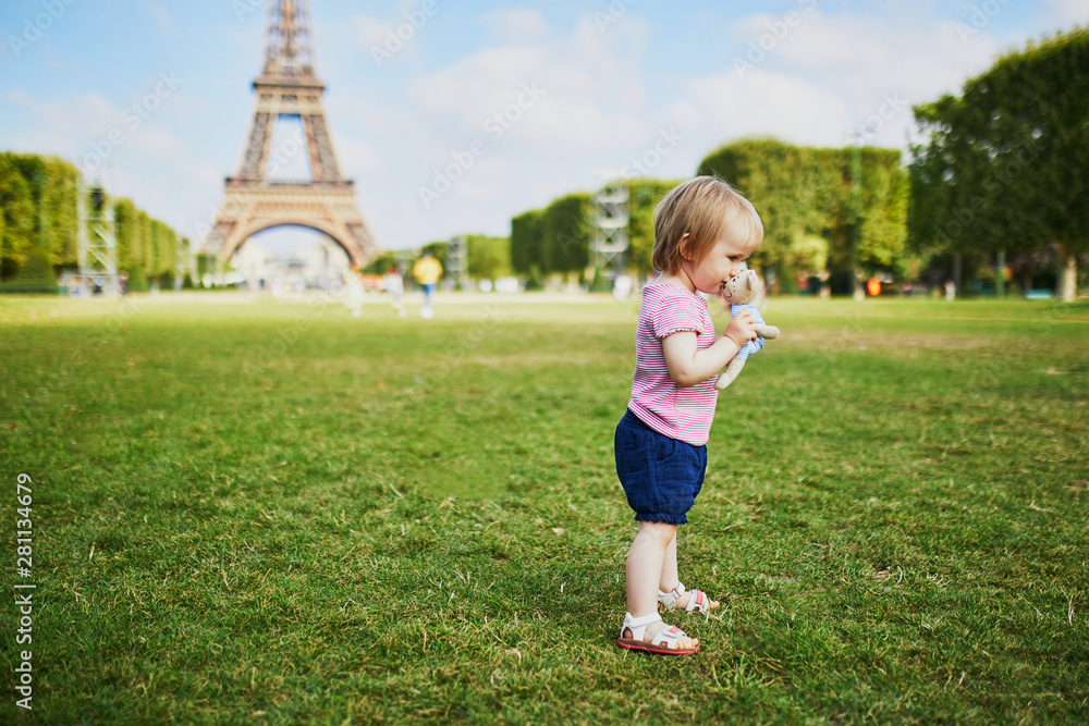 Happy toddler girl with her favorite teddy bear standing on the grass near the Eiffel tower in Paris, France Happy toddler girl with her favorite teddy bear standing on the grass near the Eiffel tower in Paris, France