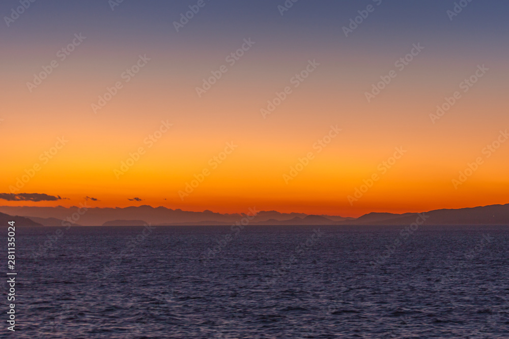 Dreamlike sunset with orange sky and islands of the Aegean Sea at horizon