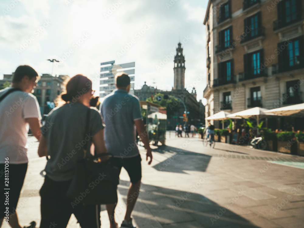 Defocused view of pedestrians men and women walking at sunset on Pas Sota Muralla street at sunset