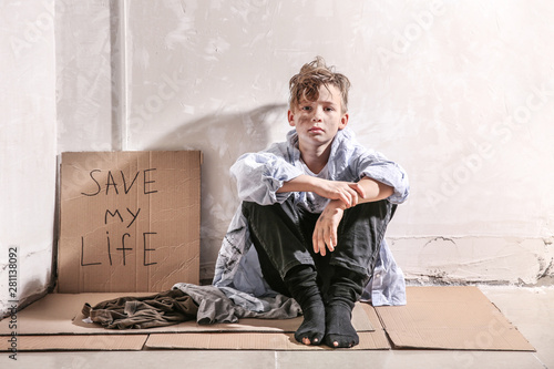 Homeless little boy sitting on floor near wall photo