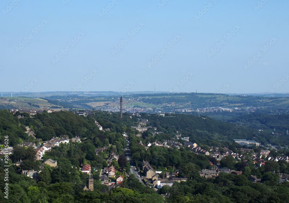 a panoramic view of the town of west yorkshire from above with streets and houses surrounded by trees and fields and the historic wainhouse tower on a hillside