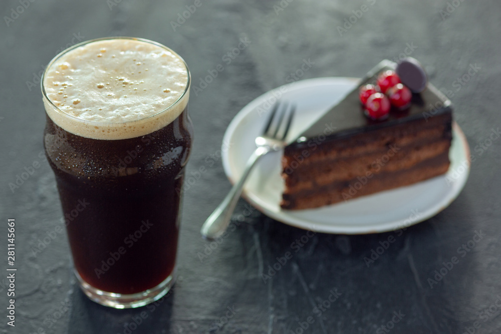 Glass of dark beer on the stone table background. Cold drink and truffles with cake are prepared for a big friend's party. Concept of drinks, fun, food, celebrating, meeting, oktoberfest. Glass of dark beer on the stone table background. Cold drink and truffles with cake are prepared for a big friend's party. Concept of drinks, fun, food, celebrating, meeting, oktoberfest.