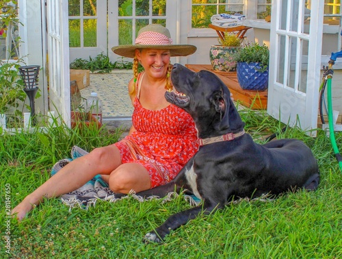Happy and Casual Mature Woman 50-59 years old hanging out with her Great Dane in her garden in front of her beautiful greenhouse