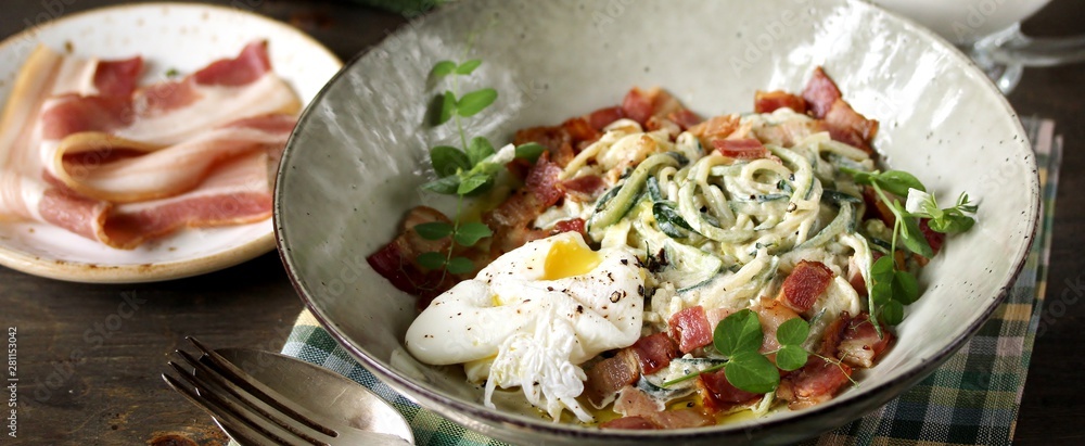 keto carbonara pasta  with spaghetti (noodles) of zucchini Low-Carb with cream, fried bacon and poached egg. decorated with pea sprouts. in a beautiful light dish. 