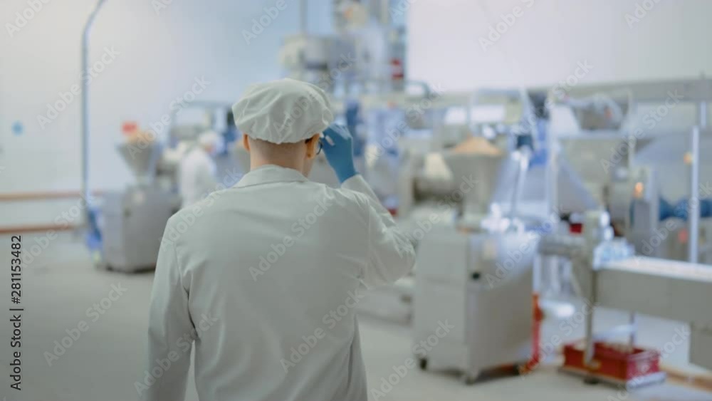 Young Male Food Employee at a Dumpling Factory Comes to Conveyor Belt. He Starts Working Together with his Colleague and Adjusts Settings on the Dash. They Wear White Sanitary Hats and Latex Gloves. Young Male Food Employee at a Dumpling Factory Comes to Conveyor Belt. He Starts Working Together with his Colleague and Adjusts Settings on the Dash. They Wear White Sanitary Hats and Latex Gloves.