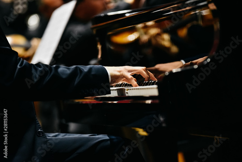 Pianist playing a piece on a grand piano at a concert, seen from the side.