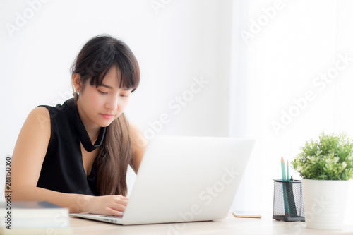 Beautiful freelance asian woman smiling working and typing on laptop computer at desk office with professional, girl using notebook checking email or social network, business and lifestyle concept. © N_studio