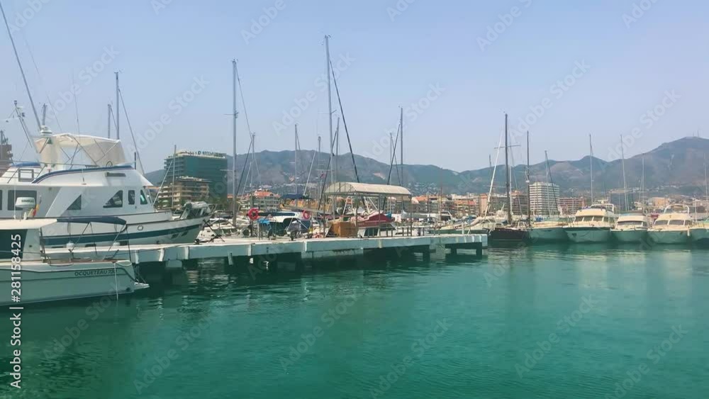 Passing moored boats in the marina in the port of Fuengirola on the Costa Del Sol in Southern Spain. A lovely serene view with the coast and mountains in the background. Passing moored boats in the marina in the port of Fuengirola on the Costa Del Sol in Southern Spain. A lovely serene view with the coast and mountains in the background.