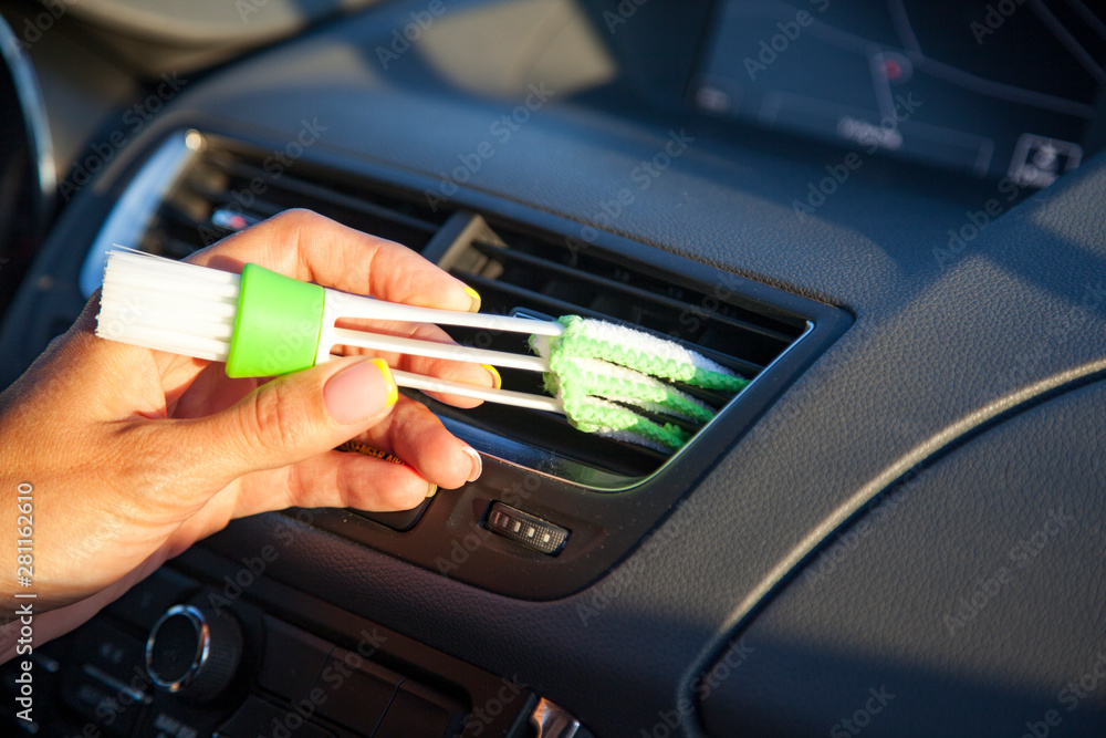 female hand with a brush for wiping dust on the dashboard of the car, a brush to remove dust in the vents from the air conditioner car