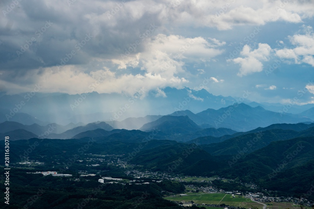 遠くの山に雲が架かり雨が降っているところを別の山から見る風景