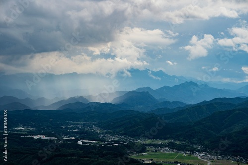 遠くの山に雲が架かり雨が降っているところを別の山から見る風景