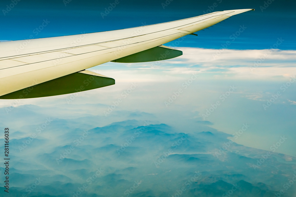Wing of plane over mountain. Airplane flying on blue sky and white clouds. Scenic view from airplane window. Commercial airline flight. Plane wing. Flight mechanics concept. International flight. Wing of plane over mountain. Airplane flying on blue sky and white clouds. Scenic view from airplane window. Commercial airline flight. Plane wing. Flight mechanics concept. International flight.